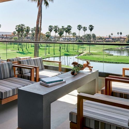 A patio features striped chairs around a stone table with a golf course view. Palm trees and water hazards are part of the scenic landscape.