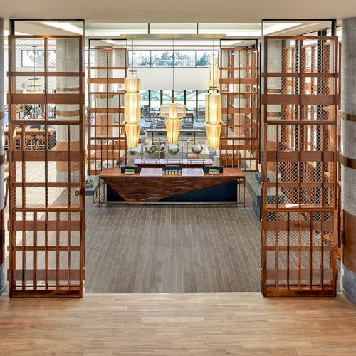 The image showcases a stylish interior featuring a modern lobby with wooden lattice panels, contemporary lighting, and a reception desk.