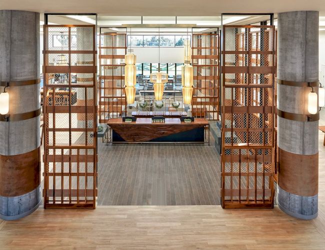 The image showcases a stylish interior featuring a modern lobby with wooden lattice panels, contemporary lighting, and a reception desk.