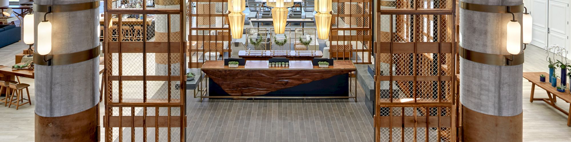 The image shows a spacious, modern lobby area with a wooden reception desk, contemporary light fixtures, and large, decorative wooden panels.