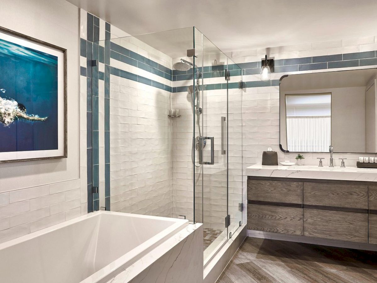 The image depicts a modern bathroom with a glass shower, bathtub, vanity with a mirror, and a picture on the wall, featuring clean, minimalist design.