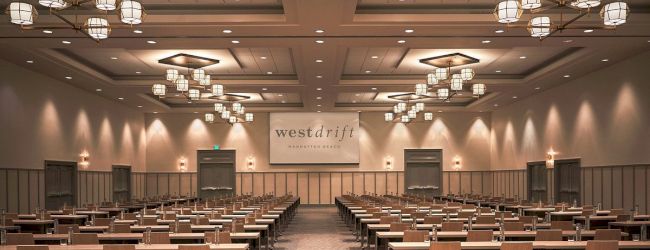 This image shows a spacious, well-lit conference room with rows of tables and chairs, and a sign that reads 