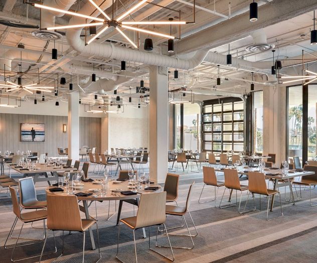 A modern, spacious dining area with wooden tables and chairs, large windows, and stylish lighting fixtures, set for a meal.