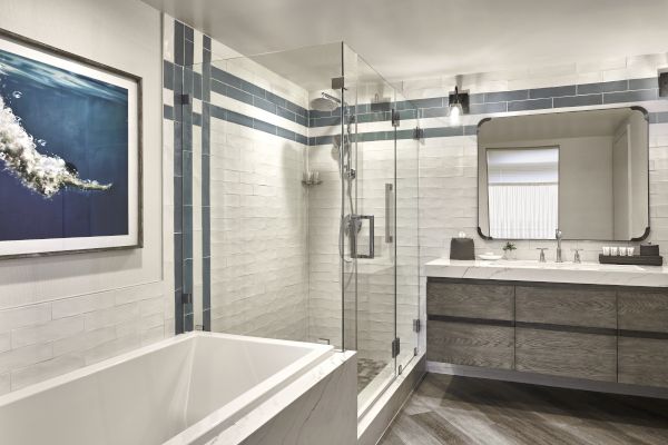 A modern bathroom featuring a bathtub, glass-enclosed shower, wall-mounted vanity with sink, mirror, and a framed picture.