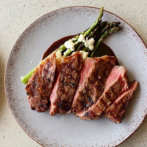 A plate with sliced steak and asparagus garnished with a sauce. The sides of another dish are visible on the left and right.