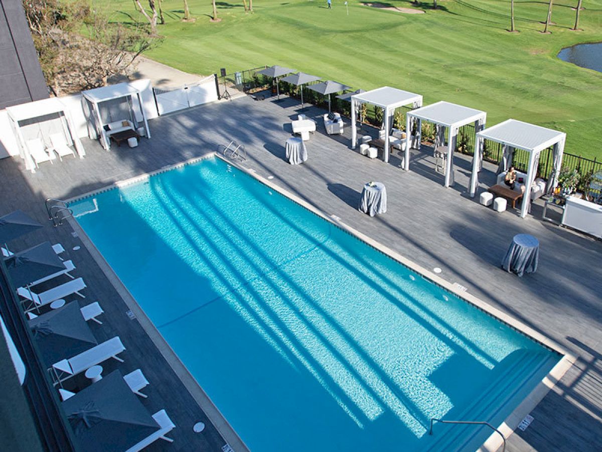 The image shows a swimming pool area with lounge chairs and cabanas, adjacent to a green golf course under sunny weather.