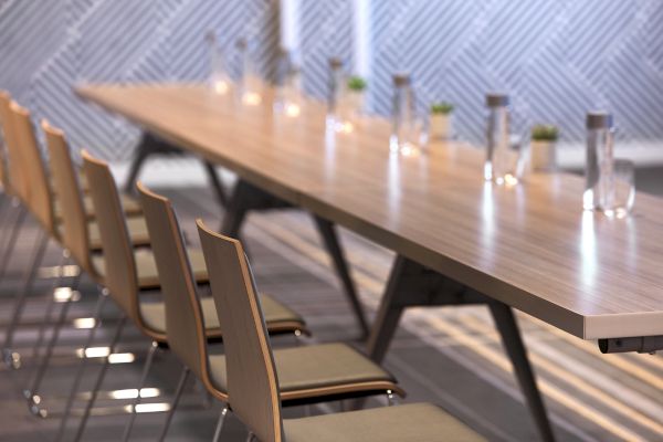 A long wooden table with chairs is neatly arranged in a modern conference room, featuring water bottles and small plants for decoration.