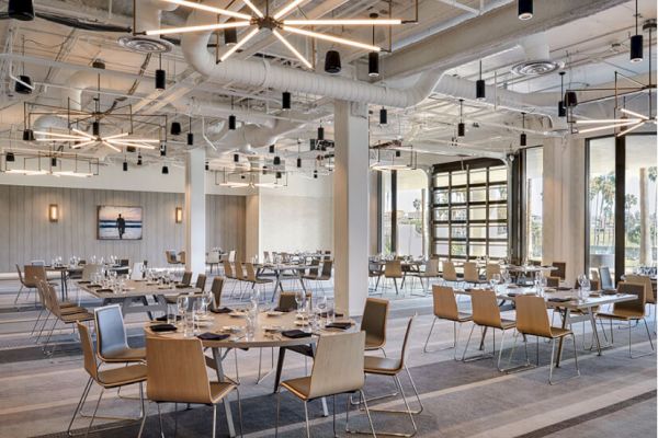 A modern dining area featuring round tables with neatly arranged table settings, contemporary lighting fixtures, and large windows.