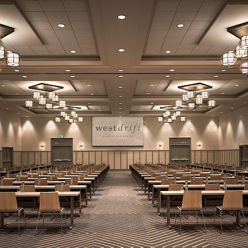 A conference room with multiple rows of tables and chairs, modern lighting fixtures, and a screen at the front displaying 