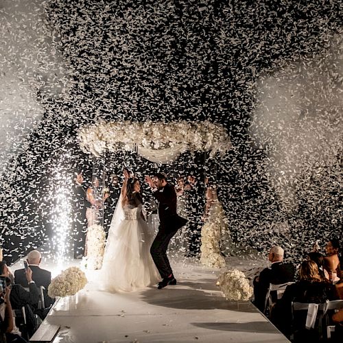 A wedding ceremony with a couple on a decorated stage, surrounded by guests, celebrating with an explosion of confetti and joyful cheers.