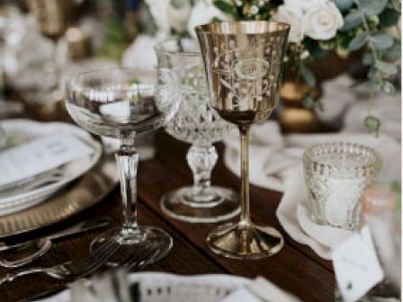 An elegantly set dining table with various glassware, a golden goblet, floral arrangements, and neatly folded napkins, exuding a sophisticated ambiance.