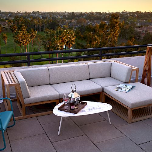 A rooftop terrace with a modern outdoor seating area, including sofas, a table, and decor, overlooking a scenic view with trees and houses in the distance.