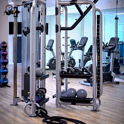 The image shows a gym with various exercise equipment, including a multi-functional machine, cardio machines in the background, and battle ropes on the floor.