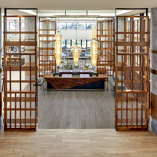 The image shows a modern, stylish lobby area with wooden panel dividers, tall pendant lights, and a reception desk in the center.