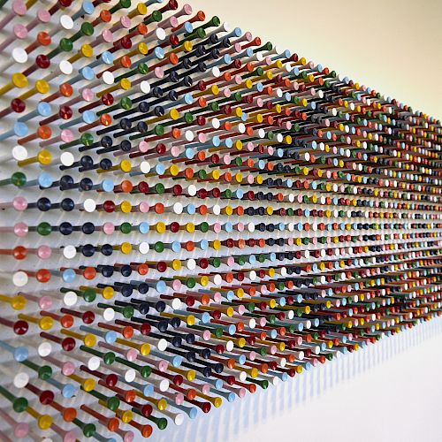 This image shows a wall installation of colorful pegs arranged in a pattern. The pegs are placed in a grid, creating a visually dynamic effect.