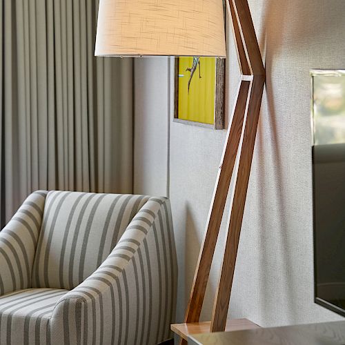 The image shows a modern interior with a striped armchair, a unique wooden floor lamp with a beige shade, and part of a TV on the right.