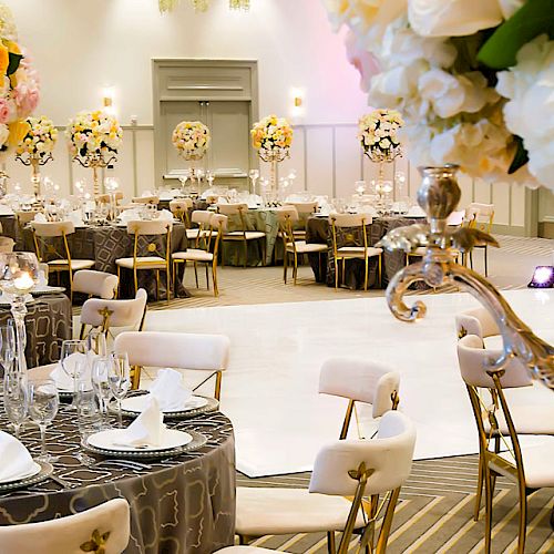 This image shows a beautifully decorated banquet hall with elegantly set tables, floral centerpieces, and a large open space for dancing or presentations.