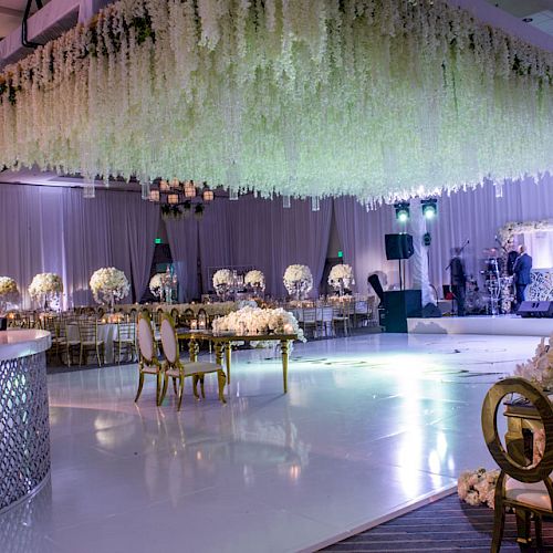 A luxurious, elegantly decorated event hall with hanging floral arrangements, lavish tables, a shiny dance floor, and stylish lighting accents.