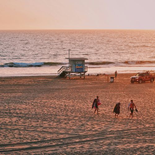 A serene beach at sunset with a lifeguard tower, a rescue vehicle, and a few people walking and enjoying the view.