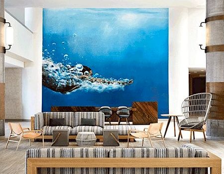 A modern lobby featuring striped sofas, accent chairs, and a striking wall mural of a sea turtle swimming underwater in vibrant blue tones.