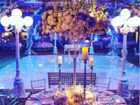 A beautifully decorated event space with elegant table settings, floral centerpieces, tall candles, and ambient lighting.