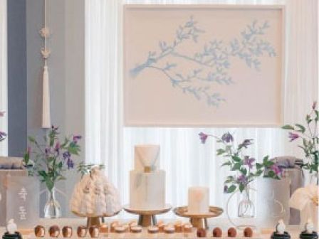 A decorative display featuring vases with flowers, candles, and assorted possibly edible items arranged on a table with a framed branch artwork above.