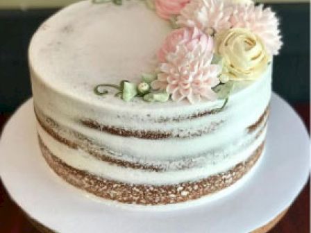 A semi-naked cake with minimal frosting, decorated with pink and white flowers on top, displayed on a white cake stand.