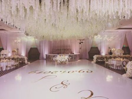 A beautifully decorated wedding venue with floral arrangements hanging from the ceiling, a white dance floor, and elegant table settings.