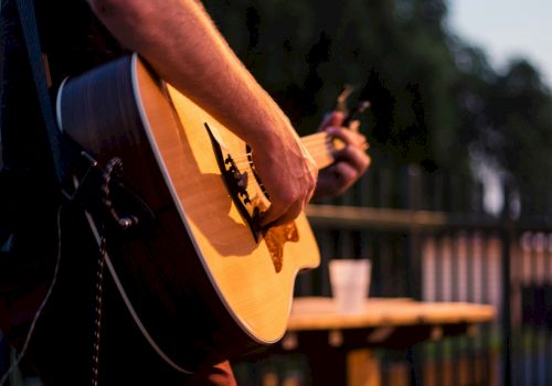 Person playing an acoustic guitar outside at dusk.