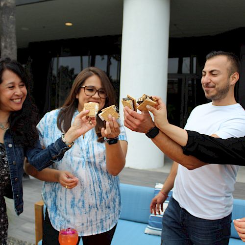 Four people are happily toasting with s'mores while standing outdoors, enjoying a casual gathering.