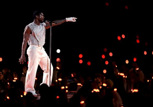 A performer in white attire sings into a microphone on stage, surrounded by an audience holding illuminated candles.