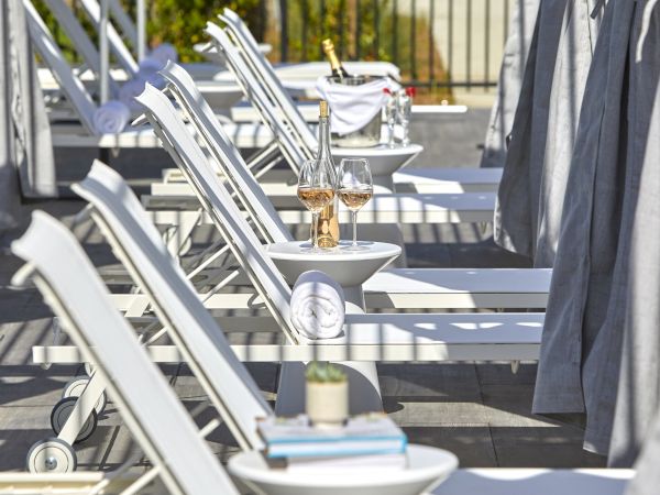 A row of white lounge chairs with small tables set with decor and towels, arranged on a sunny poolside area.